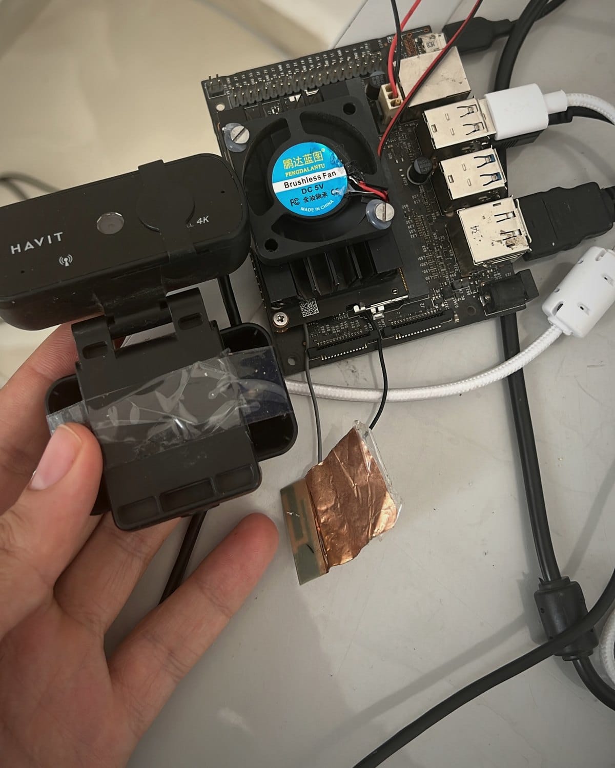 Photographie de la vraie preuve de concept EyRoad sur un établi : une NVIDIA Jetson Nano avec dissipateur et ventilateur, un câblage de prototypage et une caméra USB tenue à la main